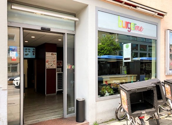 Außenansicht des burgerme Franchise-Restaurants mit offenen Eingangstüren und Lieferfahrrädern davor.