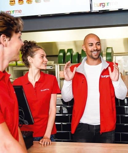 Burgerme-Mitarbeiter lächeln und sprechen hinter der Theke im Restaurant.
