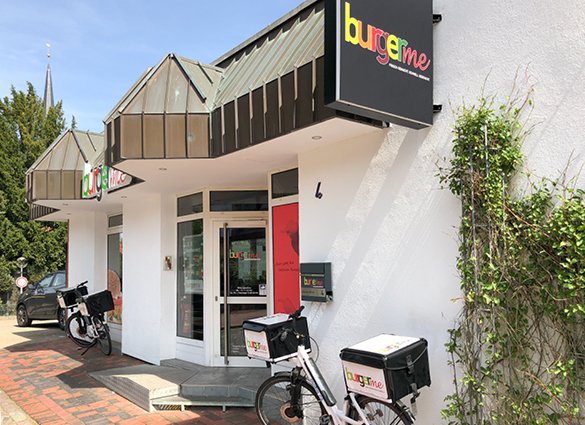 Außenansicht der burgerme Filiale mit Fahrrädern für den Lieferservice vor dem Eingang an einem sonnigen Tag.
