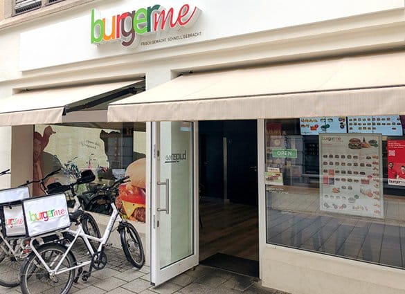Eingang eines burgerme Franchises mit geöffnetem Tür und Lieferfahrrädern davor, ideal für frische Burger-Lieferungen.