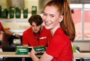 Mitarbeiterin bei burgerme lächelt im Restaurant und packt Burger ein. Perfekter Service und Qualität bei burgerme!