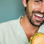 Lachender Mann genießt einen frischen Burger von burgerme – Saftiges Fleisch und knackiger Salat perfekt im Brötchen präsentiert.