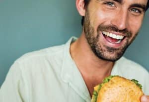 Lachender Mann genießt einen frischen Burger von burgerme – Saftiges Fleisch und knackiger Salat perfekt im Brötchen präsentiert.