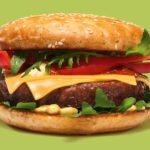 Saftiger Cheeseburger von burgerme mit Rucola, Tomaten, Käse und Sesambrötchen vor grünem Hintergrund für leckeres Fast-Food-Erlebnis