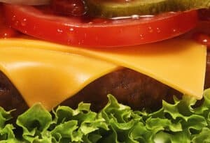 Nahaufnahme eines saftigen Cheeseburgers mit knackigem Salat, Tomaten, Käse und Essiggurken von burgerme.