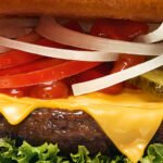 Nahaufnahme eines köstlichen Cheeseburgers mit Salat, Käse, Zwiebeln, Tomaten und Gurken von burgerme.
