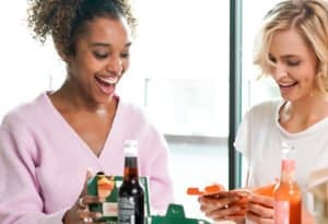 Zwei Frauen genießen ein leckeres Essen von burgerme mit Softdrinks in gemütlicher Atmosphäre.
