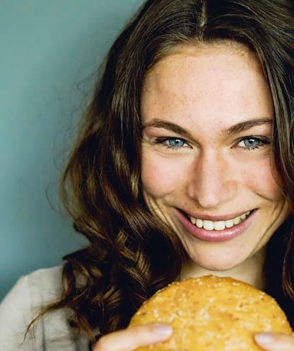 Frau mit langem Haar lächelt und hält einen Burger in der Hand – Frische und Genuss bei burgerme.