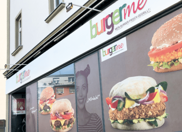 Außenansicht eines burgerme Restaurants mit Werbepostern von frisch gegrillten Burgern und dem Logo burgerme.