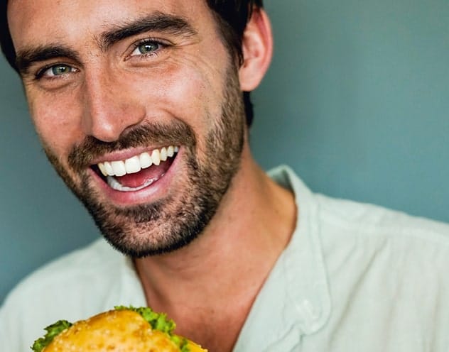 Mann hält einen leckeren Burger von burgerme und lacht. Frische Zutaten und saftiges Fleisch machen jeden Bissen zum Genuss.