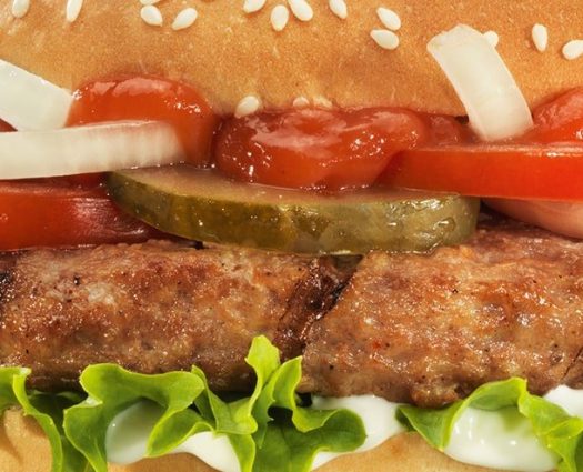 Nahaufnahme eines burgerme-Burgers mit Salat, Tomaten, Gurken, Zwiebeln, Ketchup und Sesam-Brötchen.